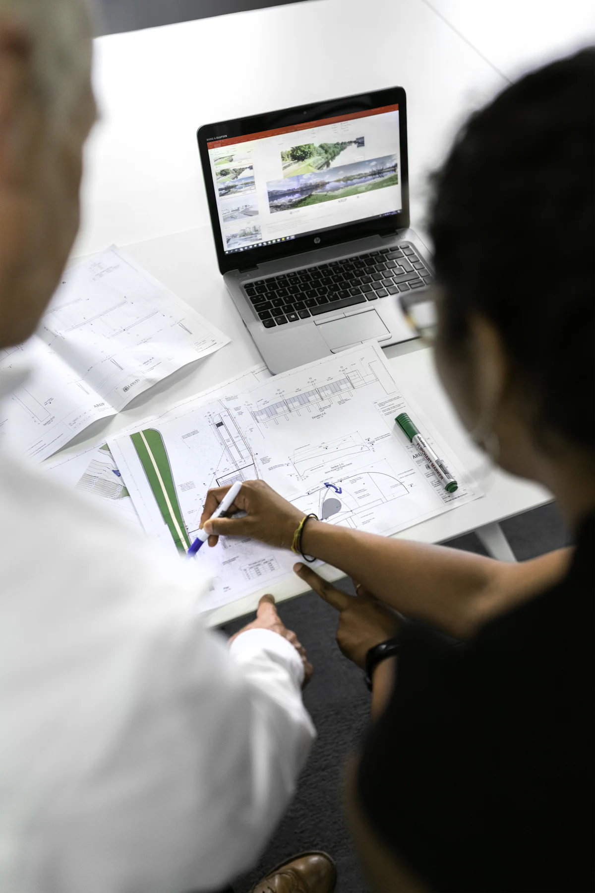 Two engineers reviewing drawings next to a laptop
